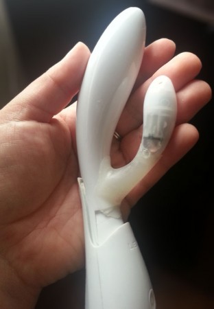Lelo Ina "deskinned" - A naked, white Lelo Ina! Photo shows a hand holding the naked Lelo Ina that has been completely deskinned of all silicone. You can see that the main insertable arm is all white, hard plastic.. The clitoral arm has a white, hard plastic tip and appears to be held on by a translucent substance. You can see some wires in the clitoral arm.