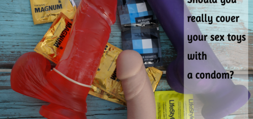 Sex toys and condoms - Should you really cover your sex toy with a condom? Shown are 3 dildos with condom wrappers, one of the dildos is a clear, red jelly dildo covered in a condom
