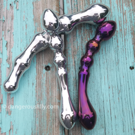 Crowned Jewels Aluminum and Anodized Titanium Sex Toys - Image shows two bright silver aluminum dildos and 1 vivid deep purple-pink anodized titanium dildo on teal distressed wood
